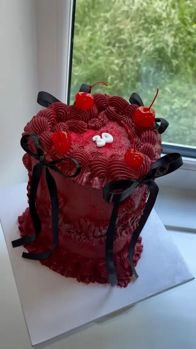 Deep red vintage cake piped with rosettes, topped with cherries and tied with black bows