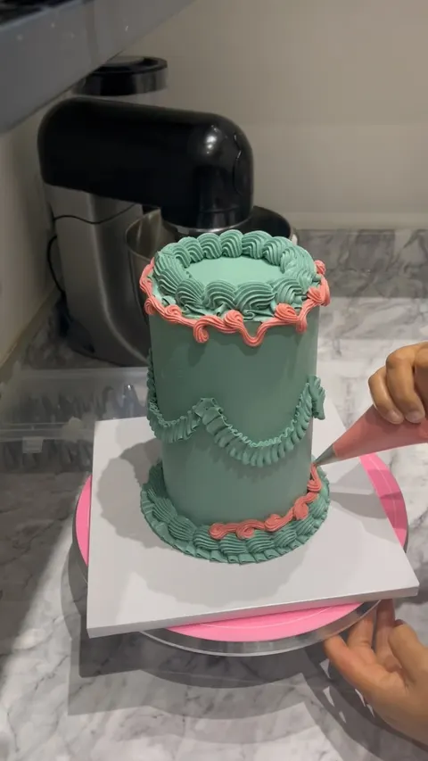 Sage green cake being piped with coral vintage borders