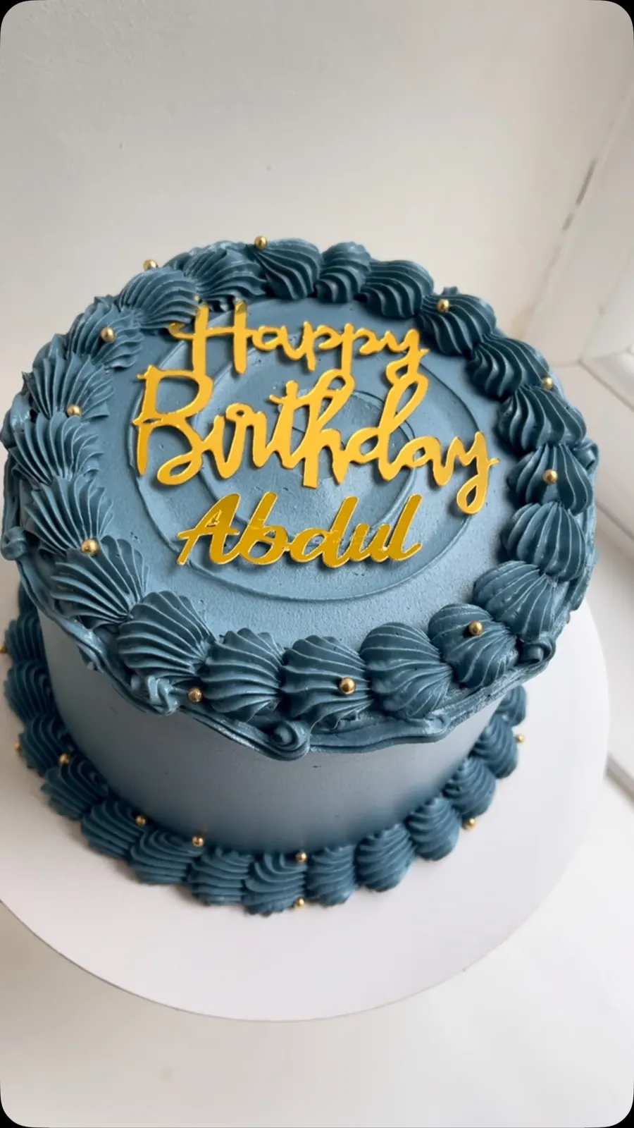 Navy buttercream cake with gold piping and a gold Happy Birthday Abdul topper, seen from above